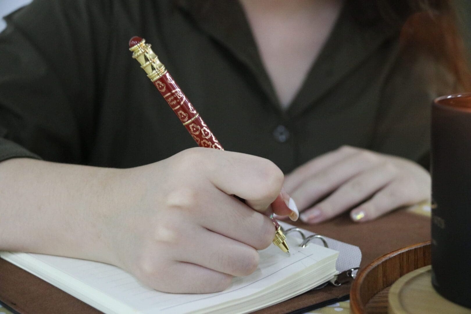 Person writing in notebook with ornate pen.
